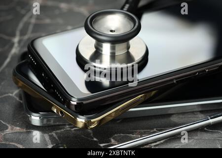 Stack of modern smartphones and stethoscope on black table, closeup Stock Photo