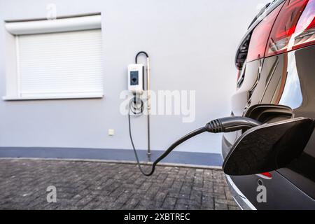 Generic electric vehicle EV hybrid car is being charged from a wallbox on a contemporary modern residential building house Stock Photo