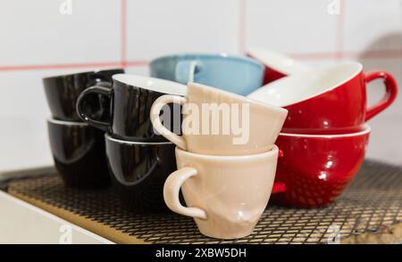Set of bright ceramic cups stand in front of white wall in caffeteria Stock Photo