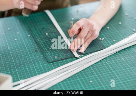 A tanner makes holes in a leather belt in a workshop. Close-up of woman's hands.  Stock Photo
