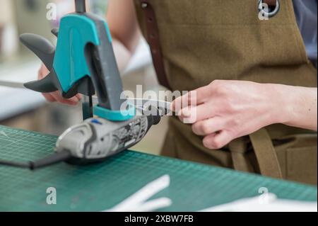 A tanner processes the edges of a leather belt in a workshop. Close-up of woman's hands.  Stock Photo