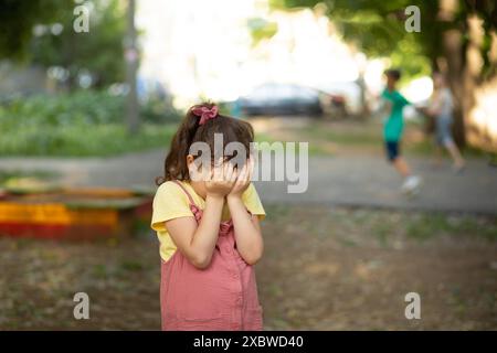 Upset lonely bullied little kid girl cries covering his eyes with his hands feels abandoned abused, sad alone preschool child in kindergarten or playg Stock Photo