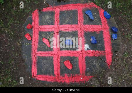 Tic-tac-toe board painted on a tree trunk with colored stones to play the game Stock Photo