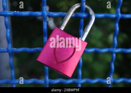 A red love padlock hanging on the blue fence of a bridge in Nordhorn Stock Photo
