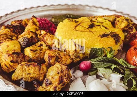 Close-up of popular Persian chicken kebab (aka jooje kabab) with saffron rice, grilled chilies and tomatoes, onions, basils, and pickled red cabbage Stock Photo