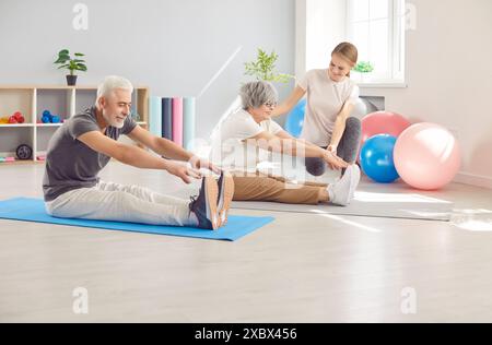 Elderly Couple Exercising With Instructor And Stretching Together In Gym Stock Photo
