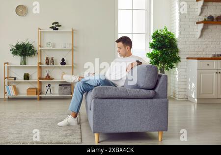 Young man in casual clothes sitting on sofa at home looking at his notepad planning daily meeting Stock Photo
