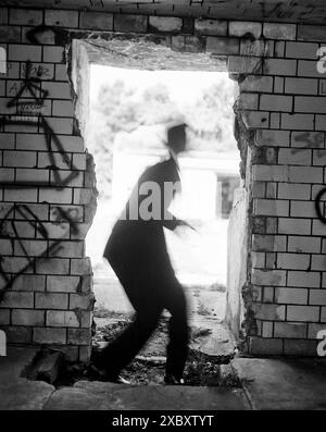 Blurred rear view of mid-adult man in suit and hat slightly crouching in open doorway Stock Photo