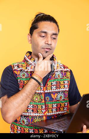 Pensive man thinking how to solve business tasks on laptop, isolated over studio background. Employee caught in brainstorming process, doing marketing analysis on notebook Stock Photo