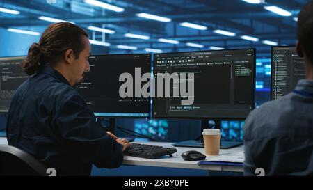 Engineers coding together in high tech server hub, using computers to analyze data, ensuring seamless data flow. Colleagues examining infrastructure in data center, ensuring system integrity and security Stock Photo