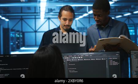Man inspecting server hub infrastructure, reading paperwork from folder, talking with workers. Supervisor doing evaluation of data center facility workspace, verifying documents Stock Photo
