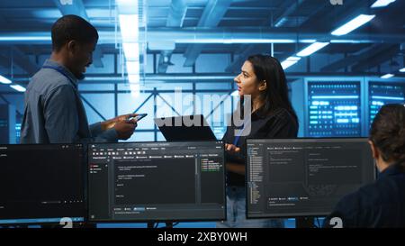 Technician and team leader in server farm looking for equipment misconfigurations affecting performance. Multiethnic coworkers checking data center infrastructure bottlenecks leading to glitches Stock Photo
