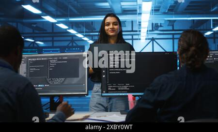 Portrait of smiling Indian manager in server room managing team of engineers looking for equipment misconfigurations. Happy team leader coordinating employees checking data center bottlenecks Stock Photo