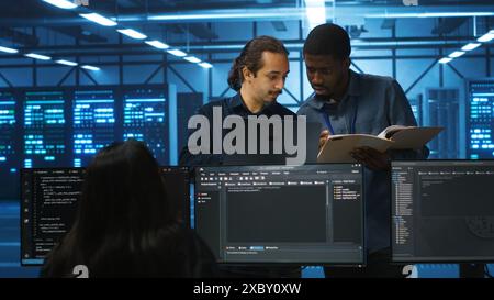 Inspector overseeing server room, reading paperwork and evaluating work done by multiracial team. Supervisor doing inspection in data center, examining hardware performance and workers output Stock Photo