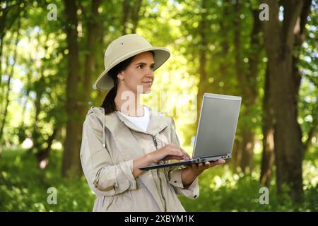Forester with laptop examining plants in forest Stock Photo