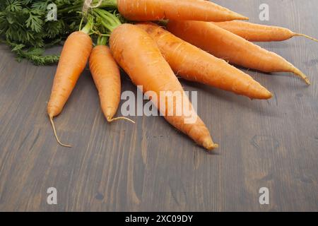 Bunch of fresh, orange carrots with green tops is neatly tied together using twine and positioned on an old, rustic wooden table Stock Photo