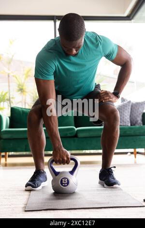 African American man lifting 8kg kettlebell at home, looking strong and fit Stock Photo