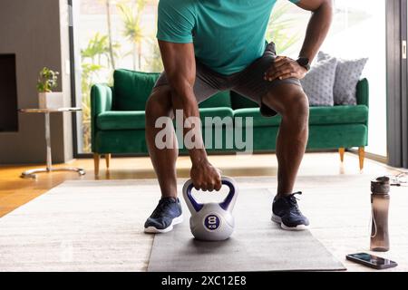 Fit African American man working out lifting 8 kg kettlebell in living room at home Stock Photo