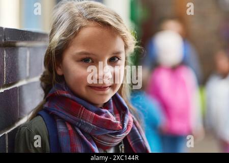 Elementary school, corridor and portrait of girl by wall for scholarship, learning and knowledge. Face, happy and student with smile in hallway for Stock Photo