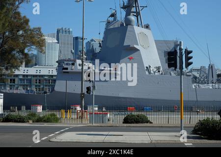 HMAS Sydney a Hobart Class guided missile destroyer (DDG) moored at Cowper Wharf, Sydney CBD Financial District skyscrapers as a backdrop Stock Photo