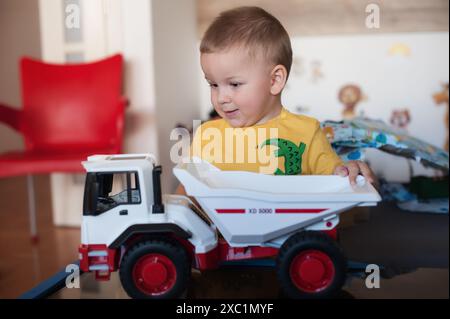 Cute little toddler plays with a toy dump truck in a home setting, smiling and enjoying driving, engross in his play. Day of imaginative fun Stock Photo
