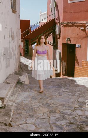 A woman in a purple top and white skirt walking in street Stock Photo