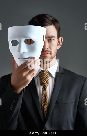 Portrait, business man and mask for secret spy in studio isolated on gray background. Fake face, suit and industrial espionage disguise of agent with Stock Photo