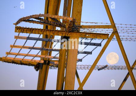 I love electricity pylons; I find their abstract, gaunt shapes endlessly fascinating. And here is a new viewpoint - a full moon seen though the upper, Stock Photo
