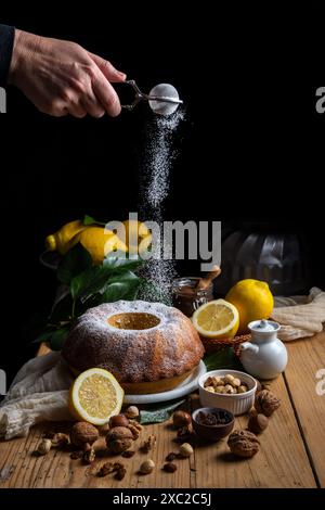 Woman's hand pouring sugar falling on bundt on table Stock Photo