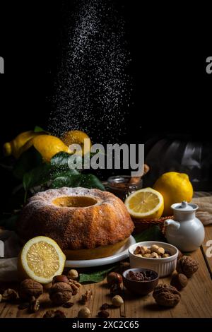 Sugar falling on bundt on table with lemons Stock Photo