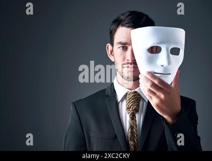 Portrait, business man and spy with mask in studio isolated on gray background. Fake face, suit and industrial espionage disguise of agent with rope Stock Photo