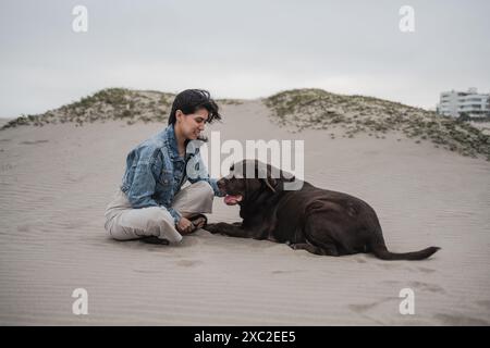 Woman Sitting with Dog on Sandy Beach Stock Photo