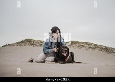 Woman Sitting with Dog on Sandy Beach Stock Photo