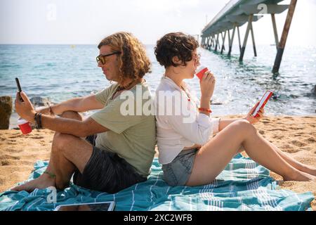 couple on the beach browsing smartphones apps. Stock Photo