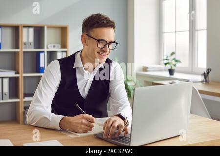 Smiling happy business man working on a laptop and looking at pc monitor screen Stock Photo