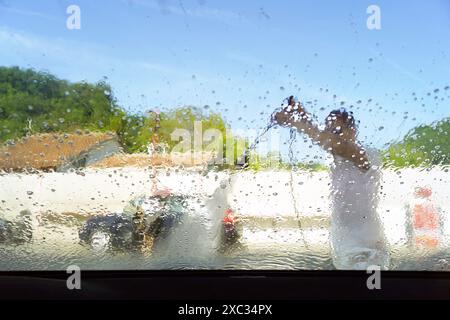 Cleaning windshield using a stream of water from a washing gun - a man washes his personal vehicle at an open-type manual car wash. Stock Photo