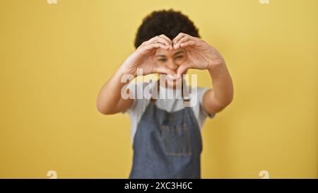 African american girl making heart gesture with hands against a vibrant yellow background wearing overalls Stock Photo