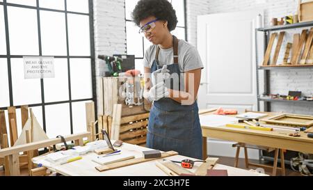 African american woman with curly hair wearing safety goggles in a carpentry workshop indoors Stock Photo