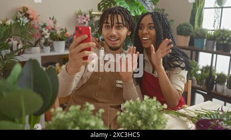 Man and woman florists having a video call in a flower shop full of plants and flowers. Stock Photo