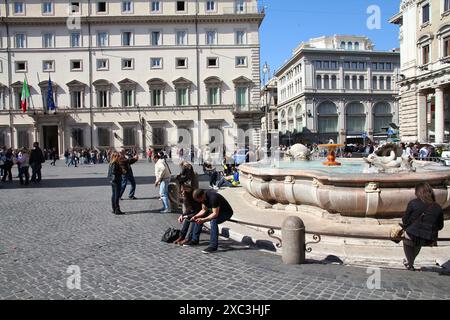 ROME, ITALY - APRIL 10, 2012: People sit by the fountain at Piazza Colonna square in Rome. According to official data Rome was visited by 12.6 million Stock Photo