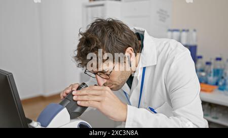 A focused hispanic man with a beard and wireless earbuds examines equipment in a lab clinic. Stock Photo