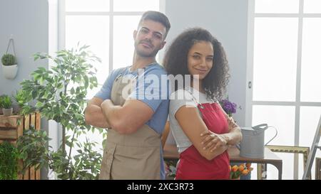 Two confident florist workers, a man and a woman, arms crossed, standing in a vibrant flower shop interior. Stock Photo