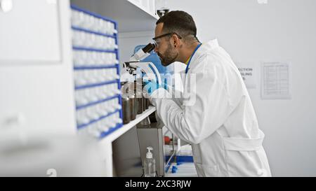 Hispanic man with beard working in laboratory analyzing samples through microscope Stock Photo
