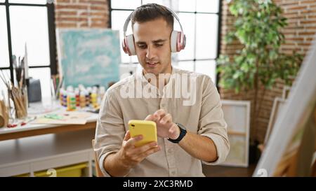 Hispanic man with headphones using smartphone indoors at an art studio. Stock Photo