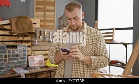 Handsome young man with beard using smartphone in a carpentry workshop room indoor Stock Photo