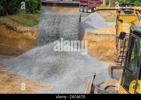 Excavator fills irregularities in excavations with granite rubble base that is then covered by concrete foundations in construction site Stock Photo