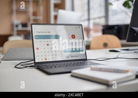 Close up shot of laptop at workplace table. Computer screen displaying calendar with month of May, focus on screen, copy space Stock Photo