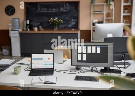 Modern office desk setup equipped with laptop displaying page of calendar and computer with app design program on screen. Functional workspace for remote learning or working, copy space Stock Photo