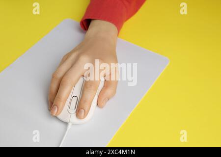 Woman using modern wired computer mouse on yellow background, closeup Stock Photo