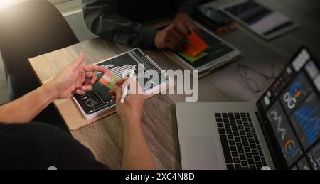 Two individuals engage in a business meeting, analyzing data displayed on tablets and a laptop. The image showcases teamwork and the use of digital to Stock Photo